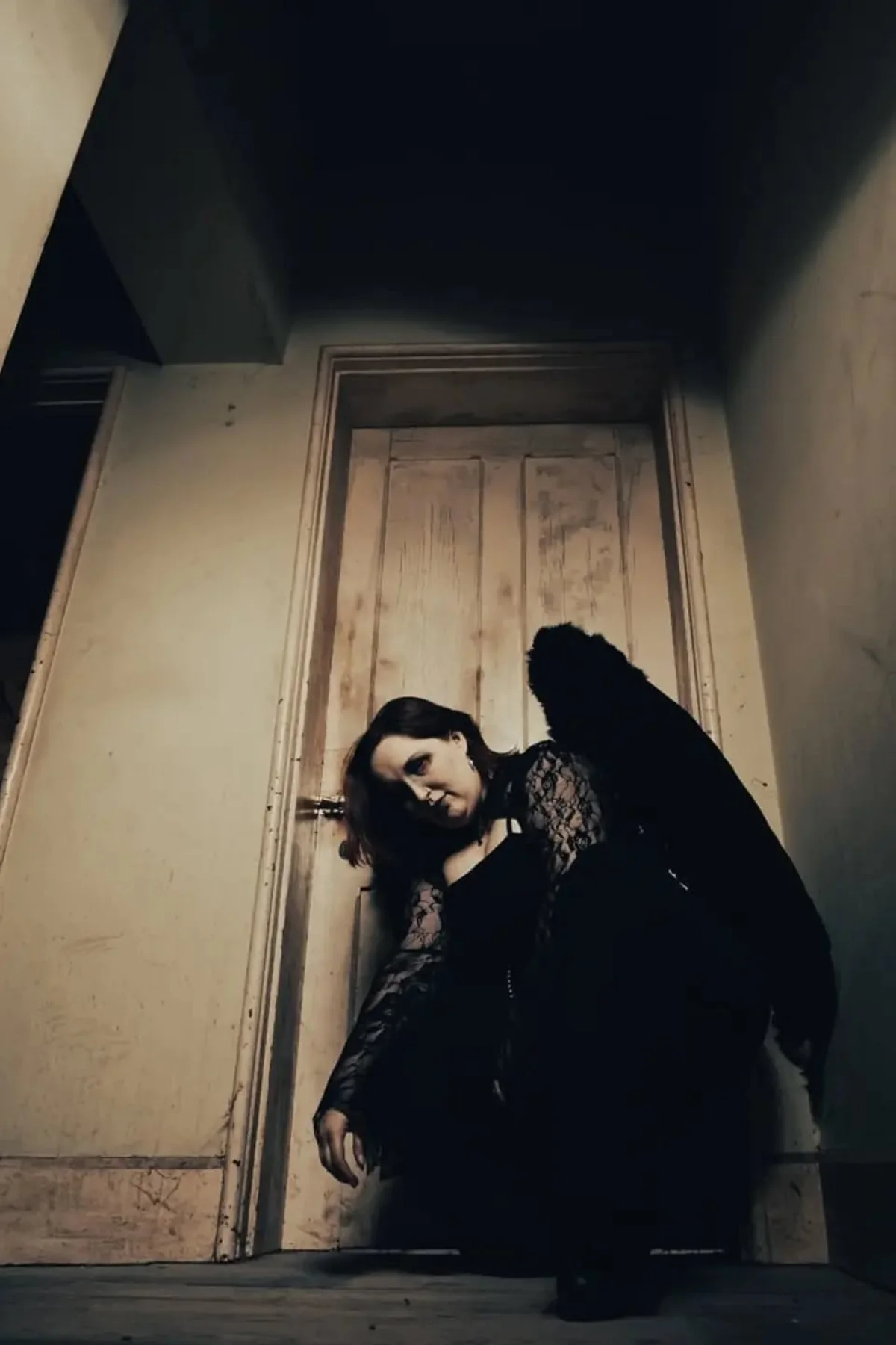 Woman in a black lace dress with large black feathered wings, a dark angel gothic Halloween costume