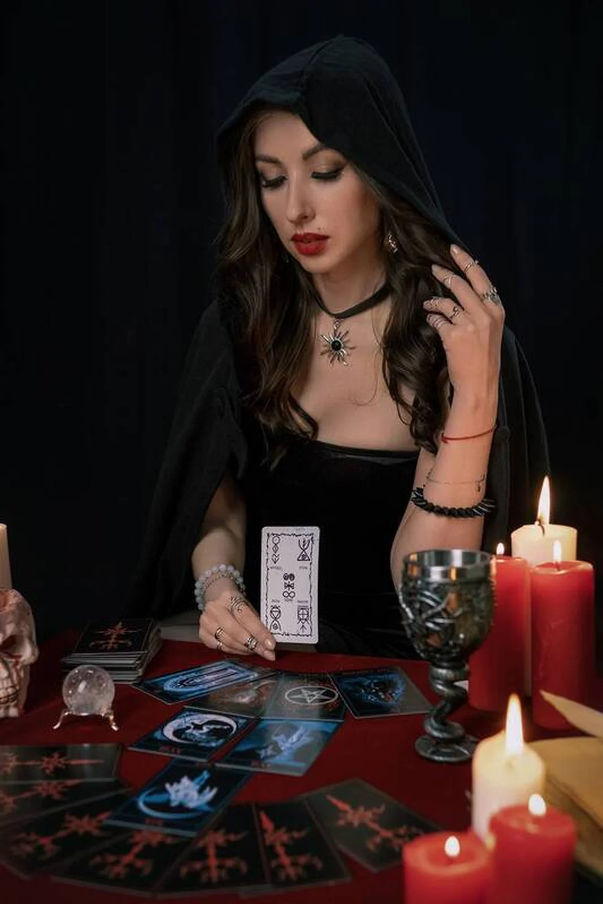 Woman in a black hooded dress reading tarot cards by candlelight, a gothic fortune teller gothic Halloween costume