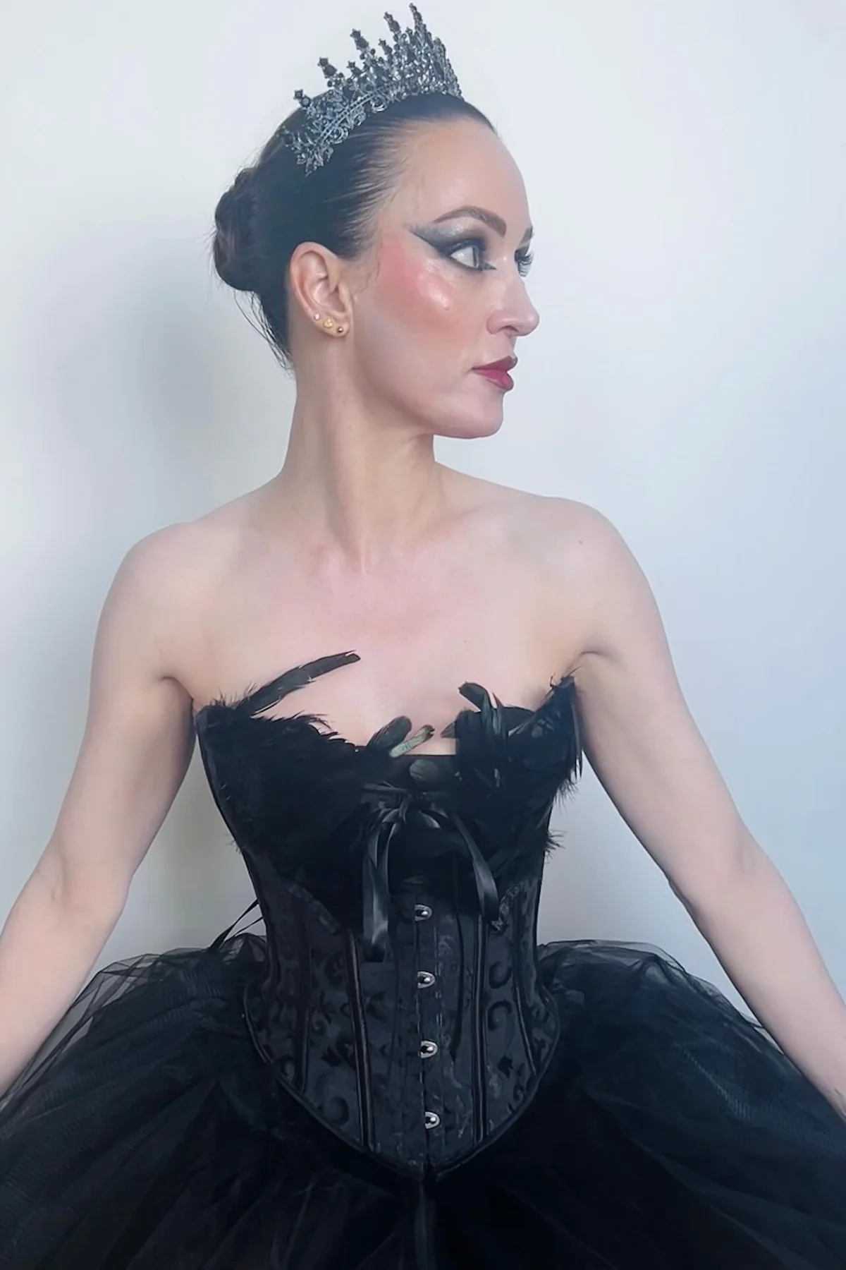 Woman in a black feather-trimmed corset bodice and voluminous black tulle skirt with a crown, a black swan ballerina gothic Halloween costume