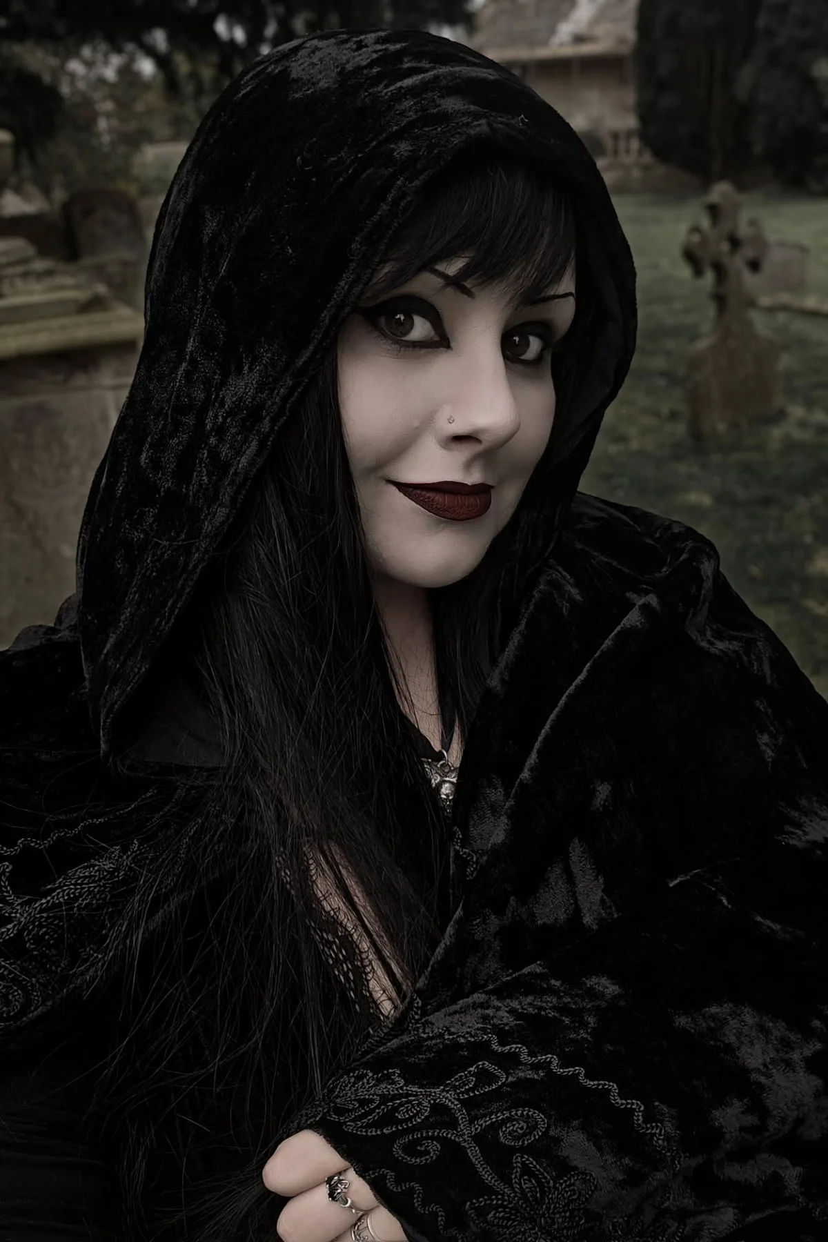 Woman in a floor-length black velvet hooded cloak with a skull pendant in a cemetery, a night owl darkling gothic Halloween costume