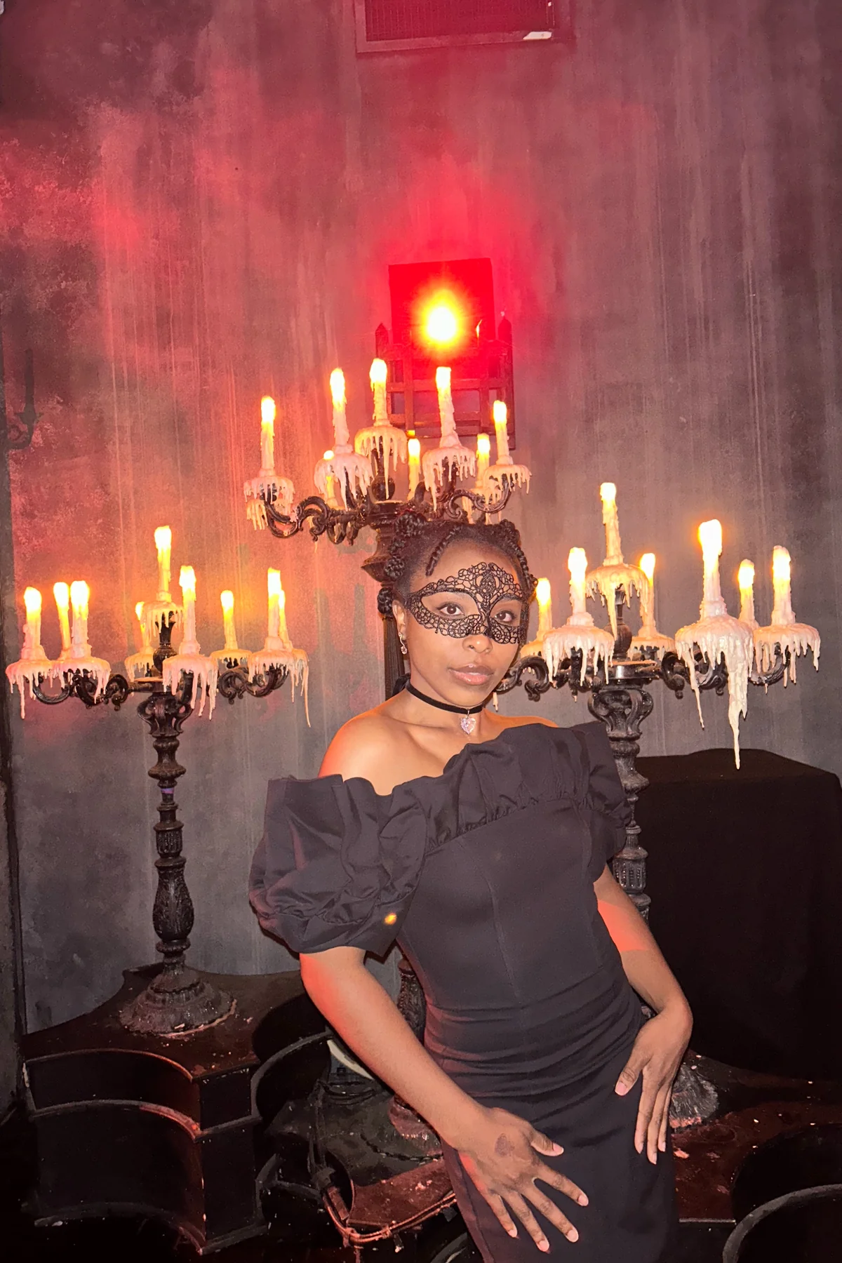Woman in a black off-shoulder dress with a black lace eye mask and choker, a phantom opera guest gothic Halloween costume