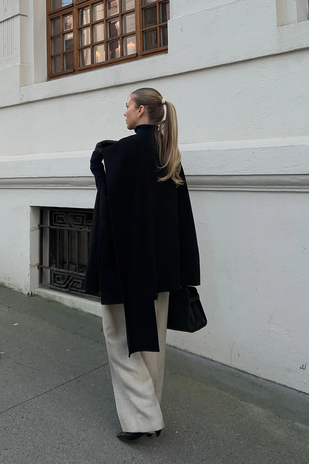Woman in a black cape coat and wide-leg trousers, a dramatic gothic Halloween costume