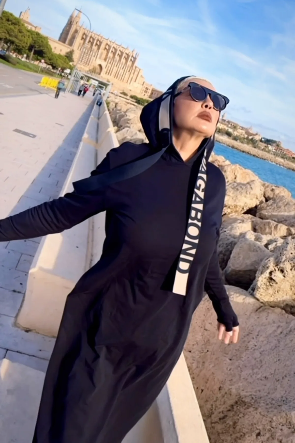 Woman in a hooded black tunic and tall boots, an easy gothic Halloween costume for travel