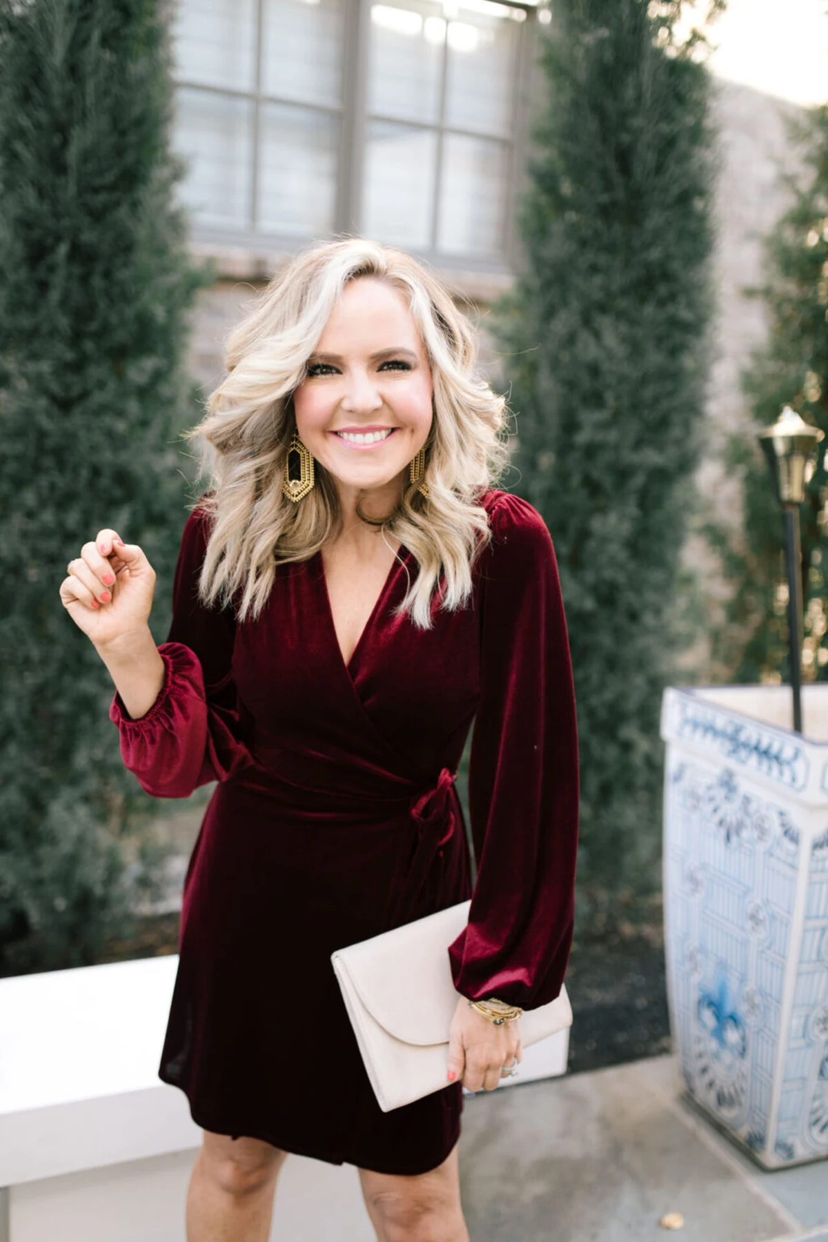 Woman in a burgundy velvet wrap dress with blouson sleeves on a porch at Christmas