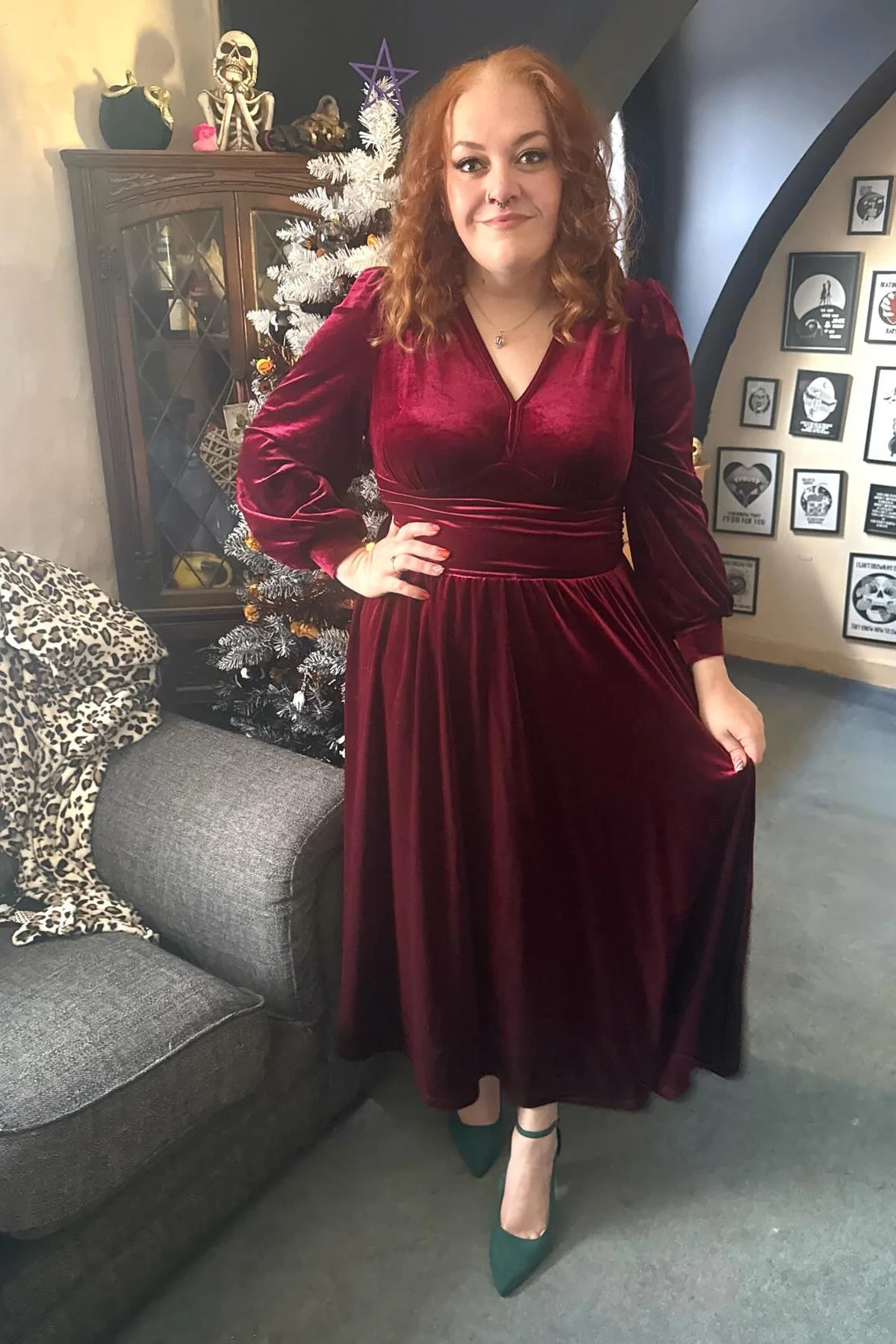 Woman in a burgundy velvet midi dress with balloon sleeves beside a flocked Christmas tree