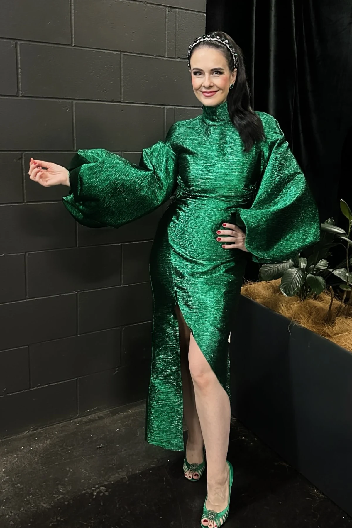 Woman in an emerald high-neck midi dress with balloon sleeves and green heels