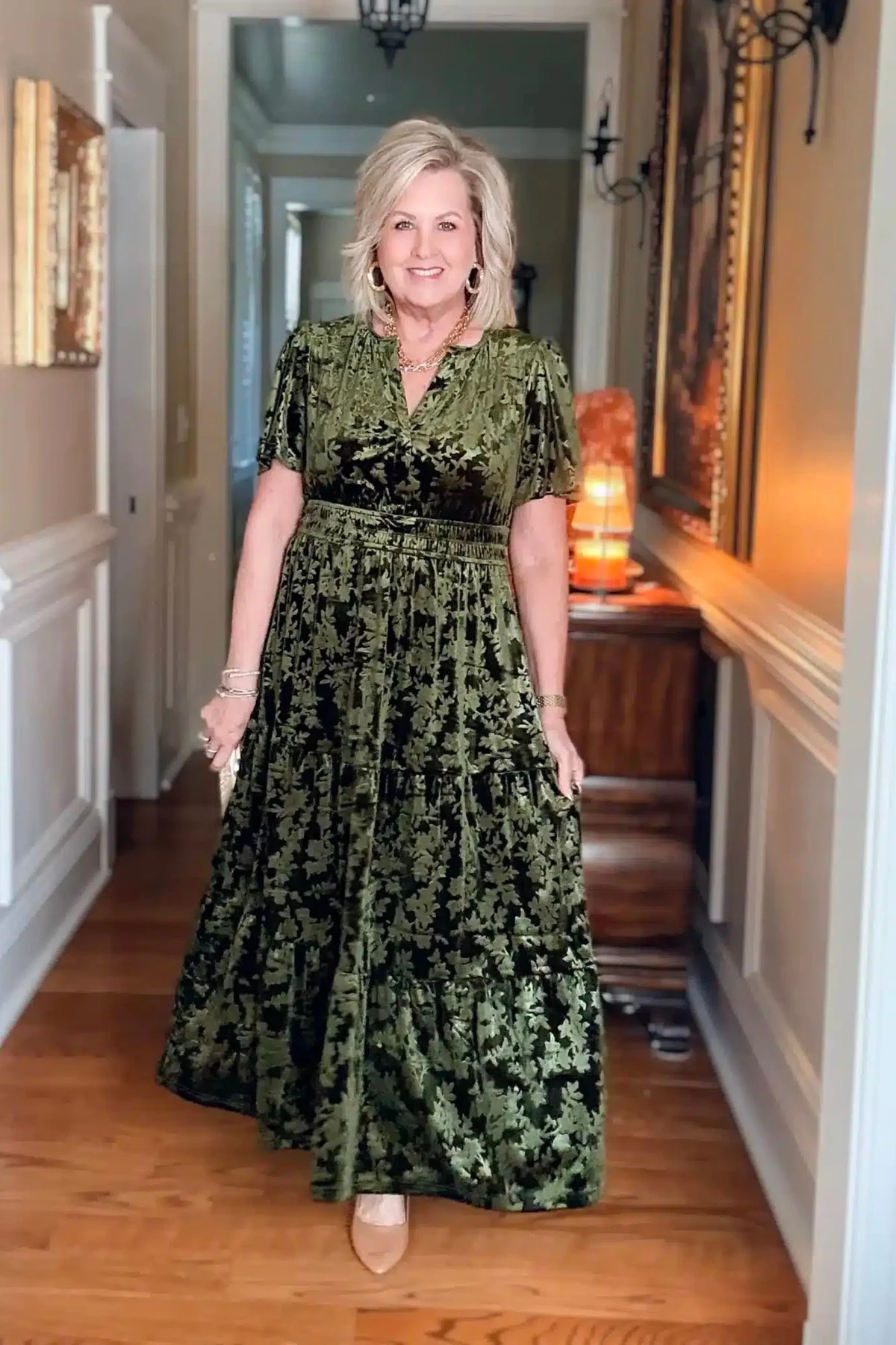 Woman in a green velvet burnout maxi dress with flutter sleeves in a warmly lit hallway