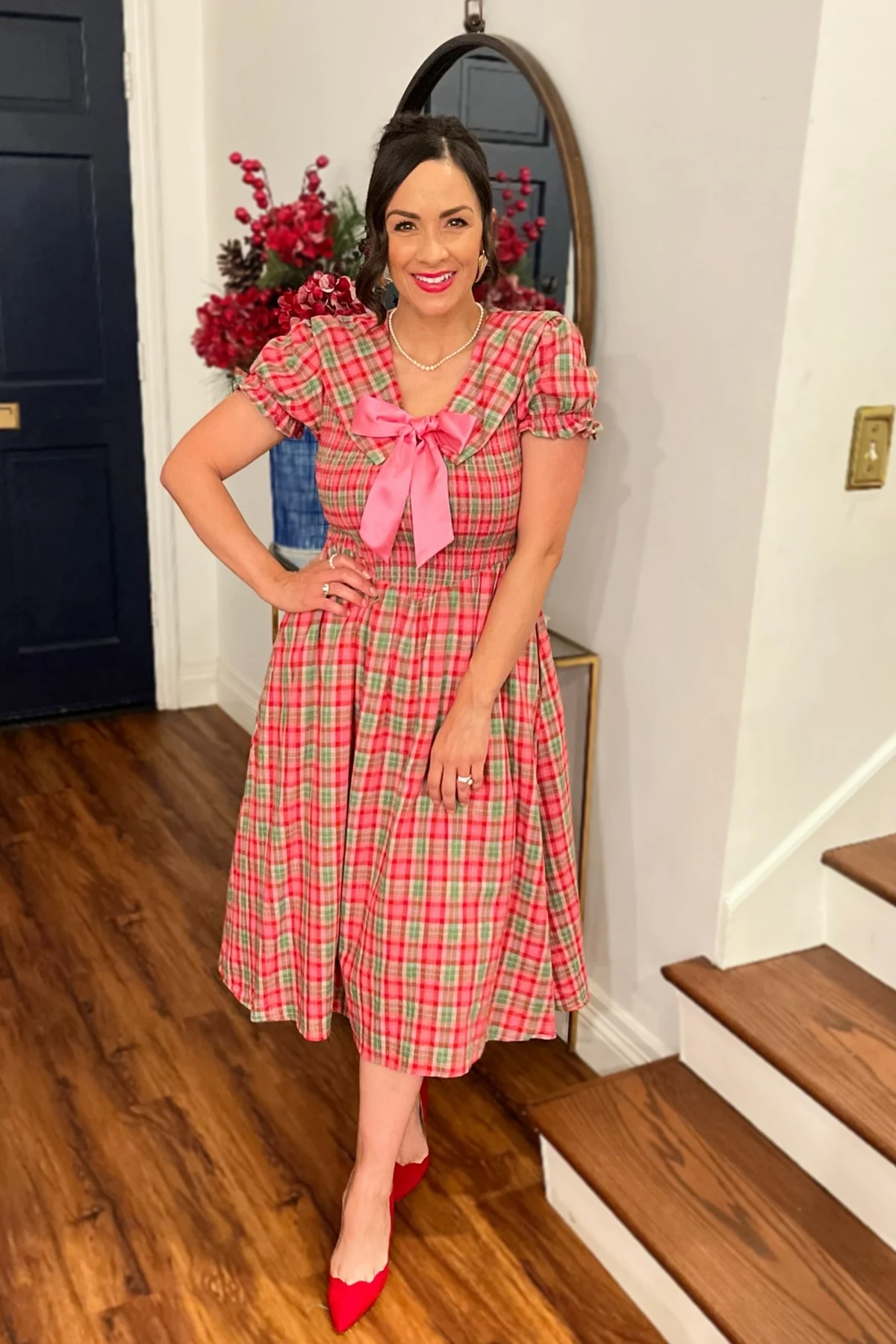Woman in a red and green plaid midi dress with puff sleeves and a pink satin bow