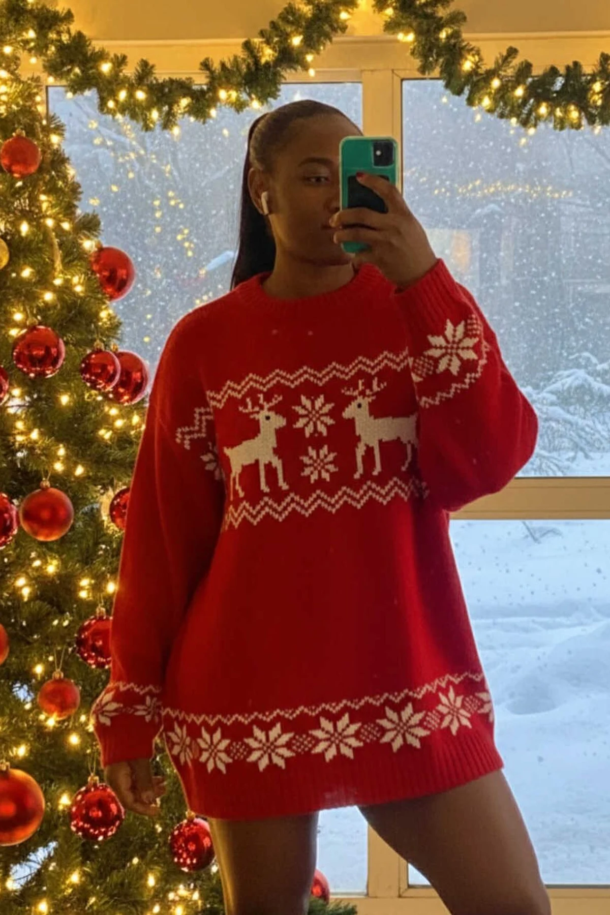 Woman in a red Fair Isle knit sweater dress with long sleeves beside a Christmas tree