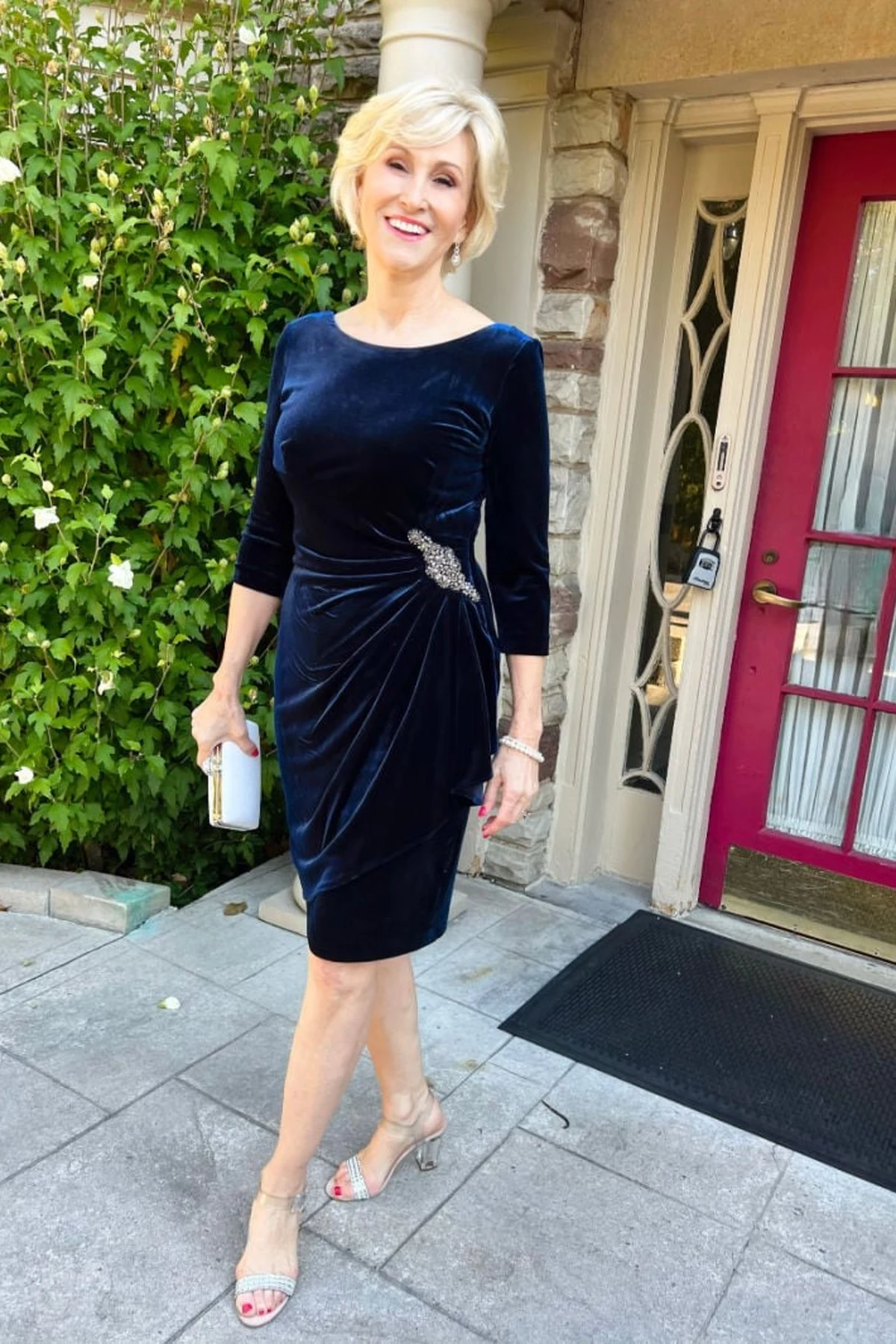 Woman over 50 in a navy velvet cocktail dress with three-quarter sleeves and a crystal brooch