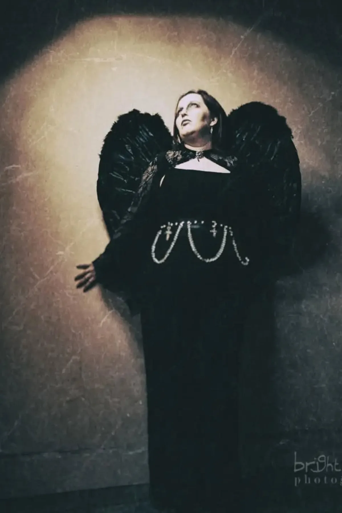 Woman in a black slip dress with black feather wings and a dark halo, a fallen angel solo Halloween costume