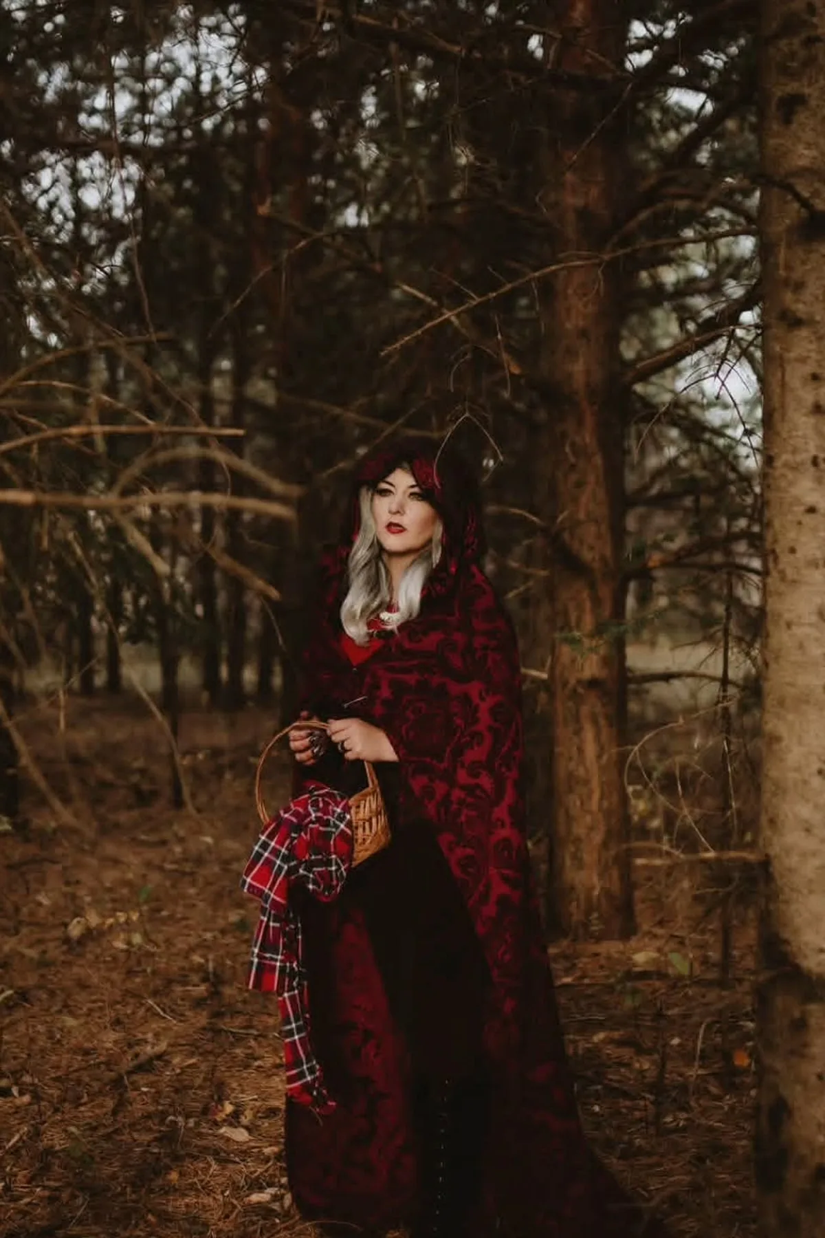 Woman in a red hooded cloak and black midi dress carrying a wicker basket, a dark Red Riding Hood solo Halloween costume