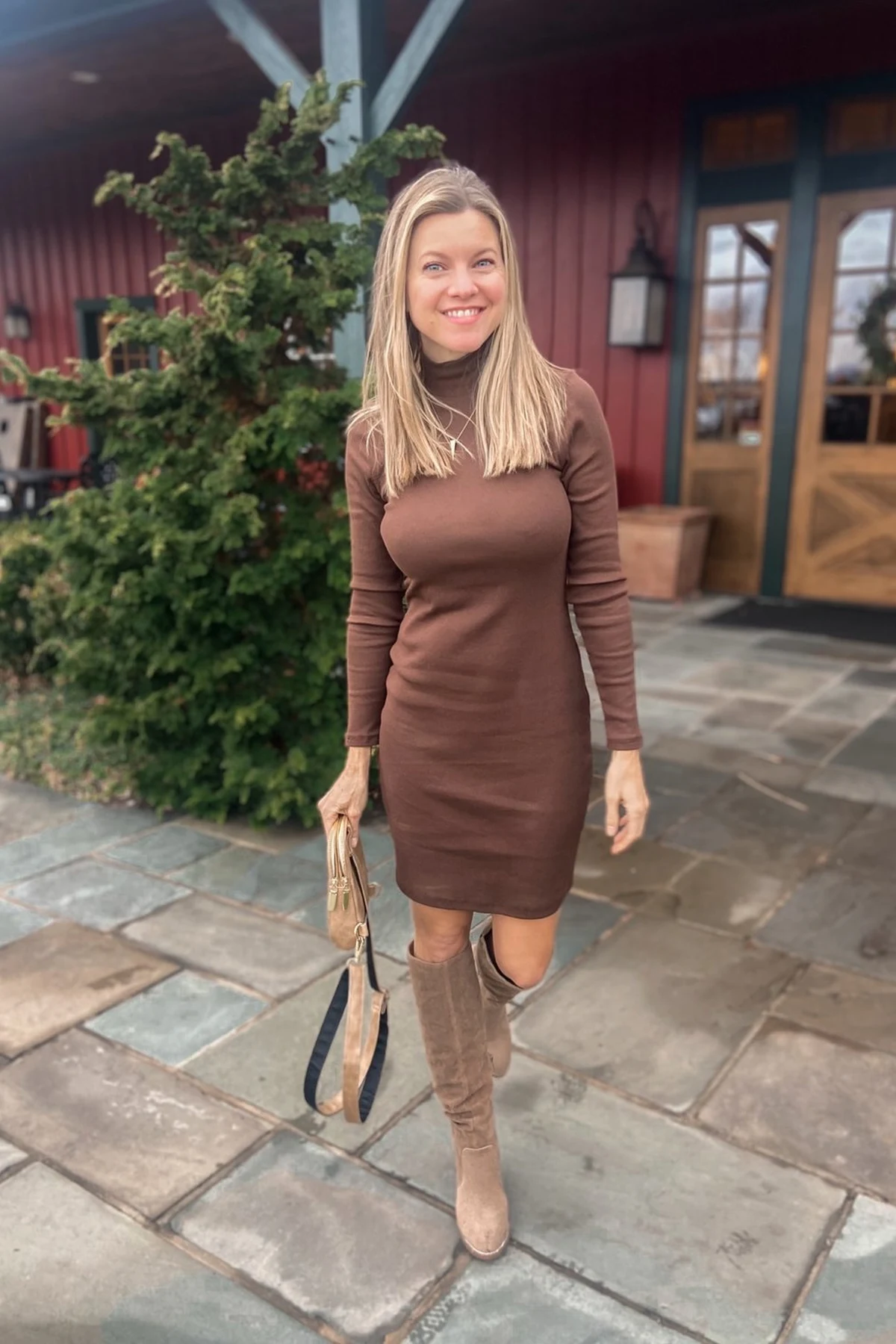 Woman in navy knit tunic dress, leggings and tall boots at a train station at Christmas