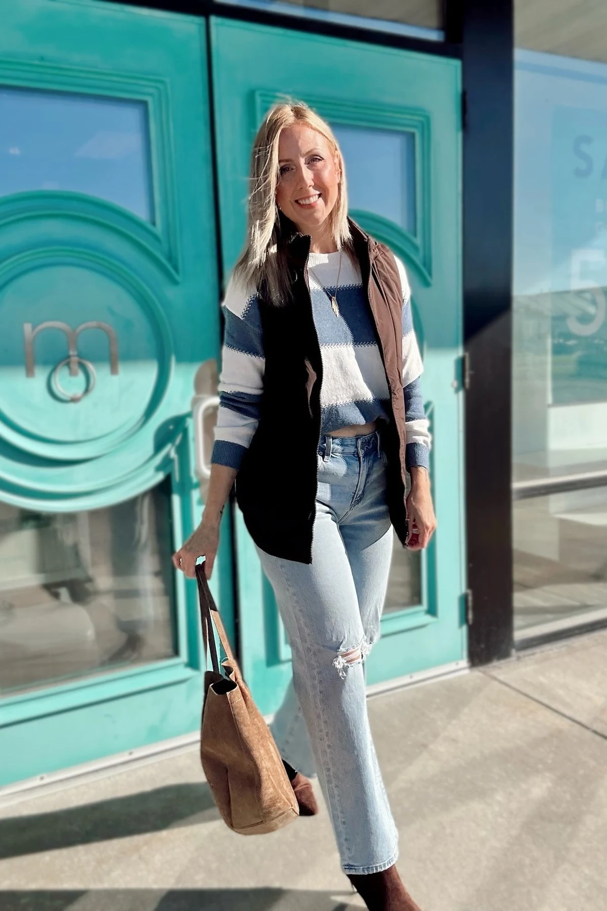 Woman in black puffer vest, striped sweater and dark jeans loading a suitcase for a road trip