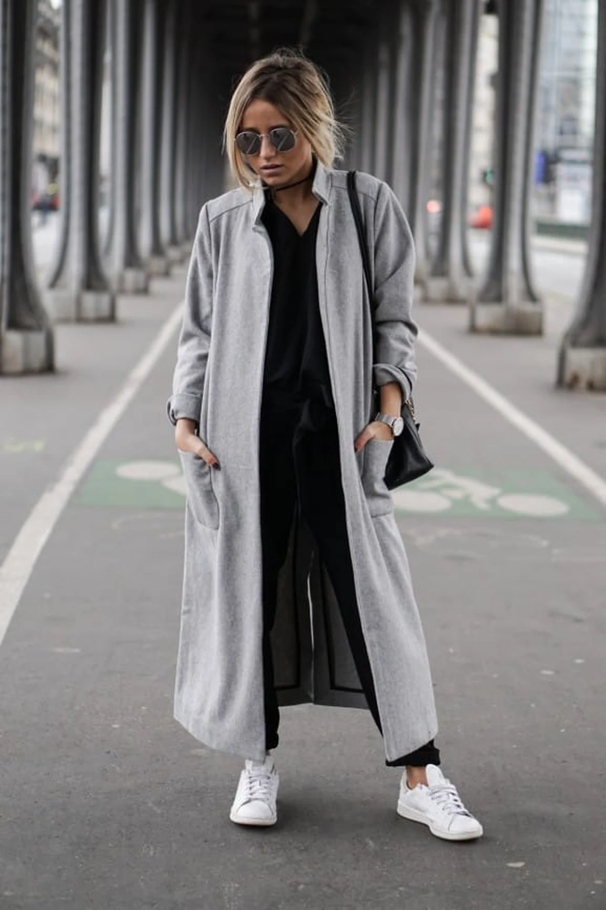 Woman in gray trench, black knit top and wide-leg jeans in an airport walkway at Christmas