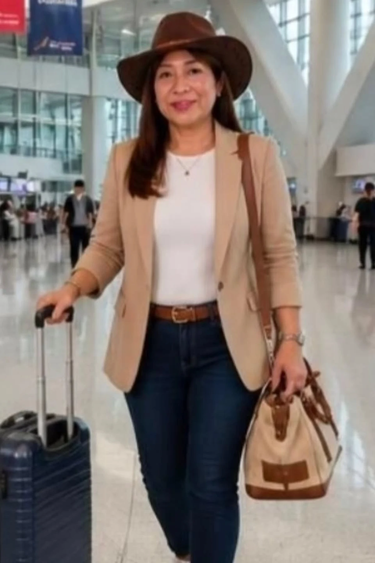 Woman in camel knit blazer, white tee and dark jeans pulling a carry-on at Christmas