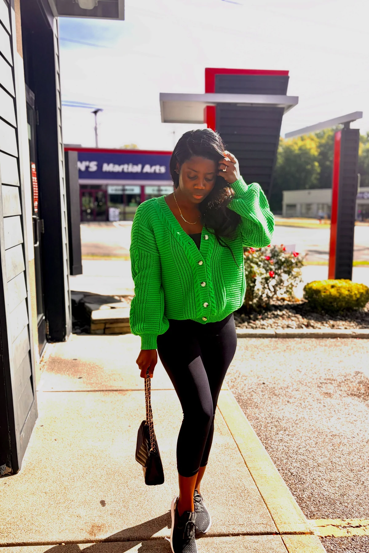 Woman in green long cardigan, black tee and gray joggers on a bench with coffee