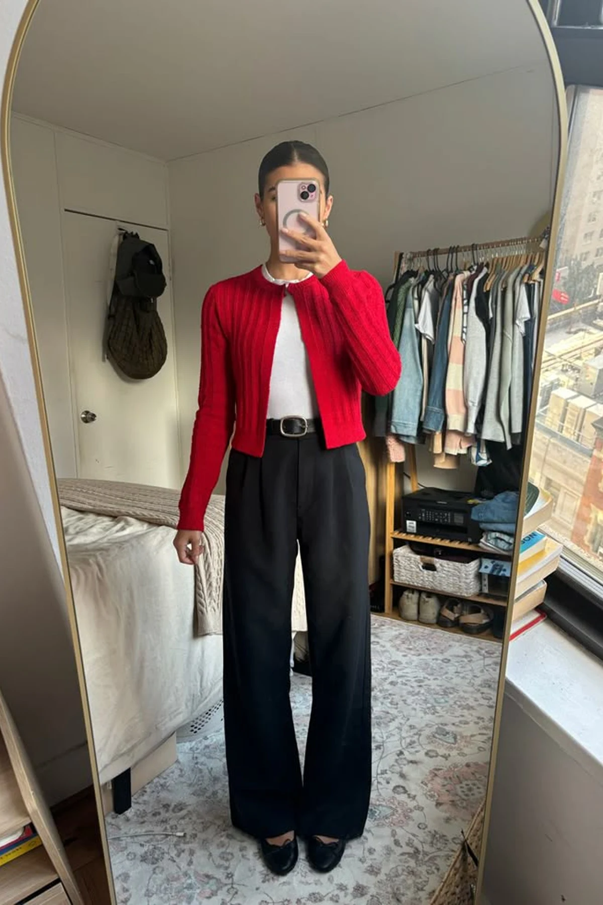 Woman in red wrap cardigan and black straight pants in an airport terminal with a Christmas tree