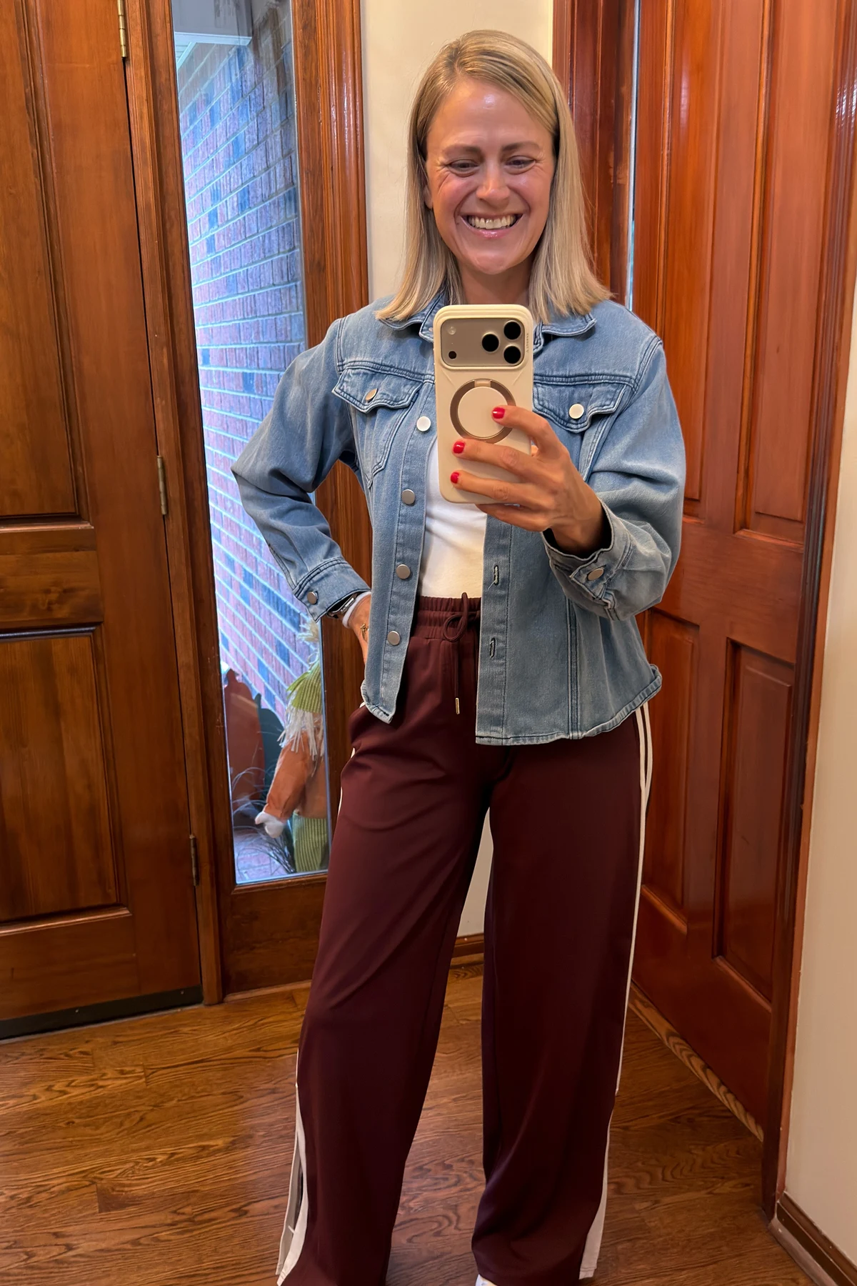 Woman in cream sweater, burgundy joggers and denim jacket in a station with a Christmas tree