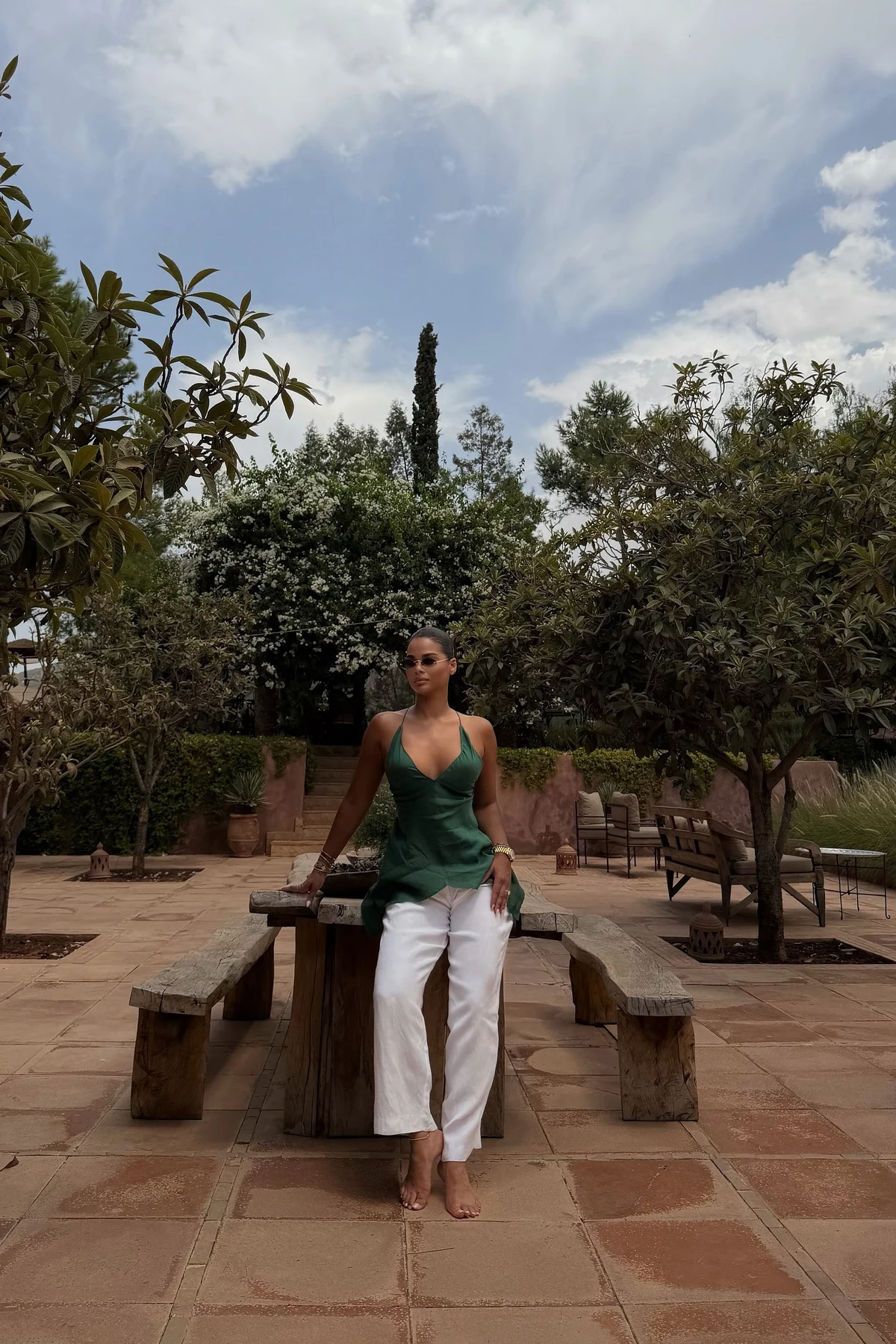 Woman in white linen wide-leg pants and emerald tank on a sunny patio at Christmas