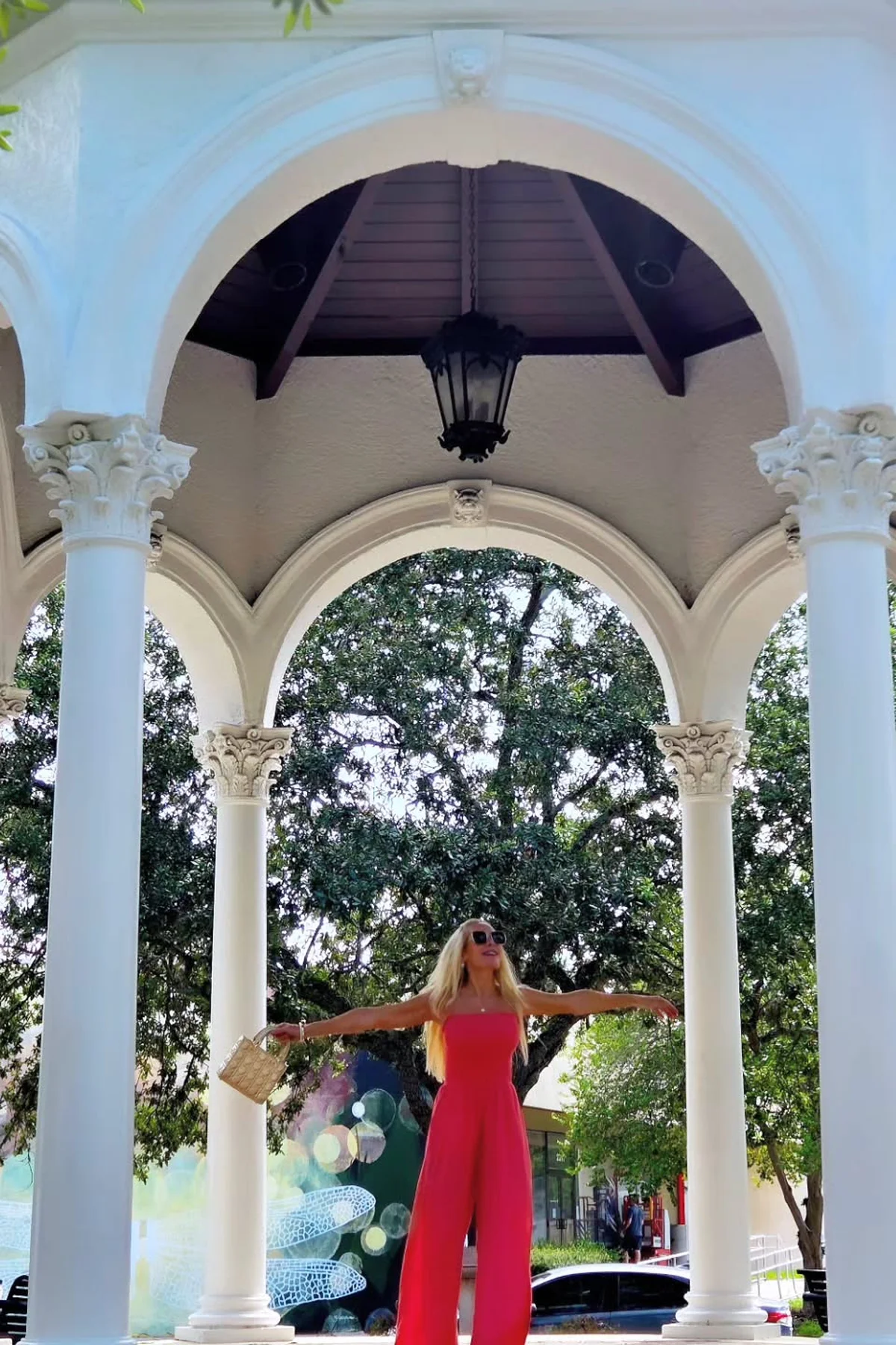 Woman in red linen jumpsuit and tan sandals in a sunny courtyard at Christmas
