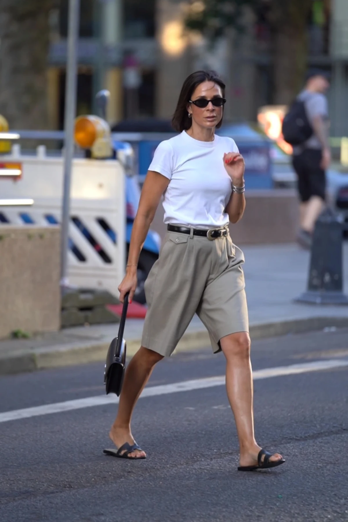 Woman in white linen shirt and khaki Bermuda shorts carrying a gift on a beach path