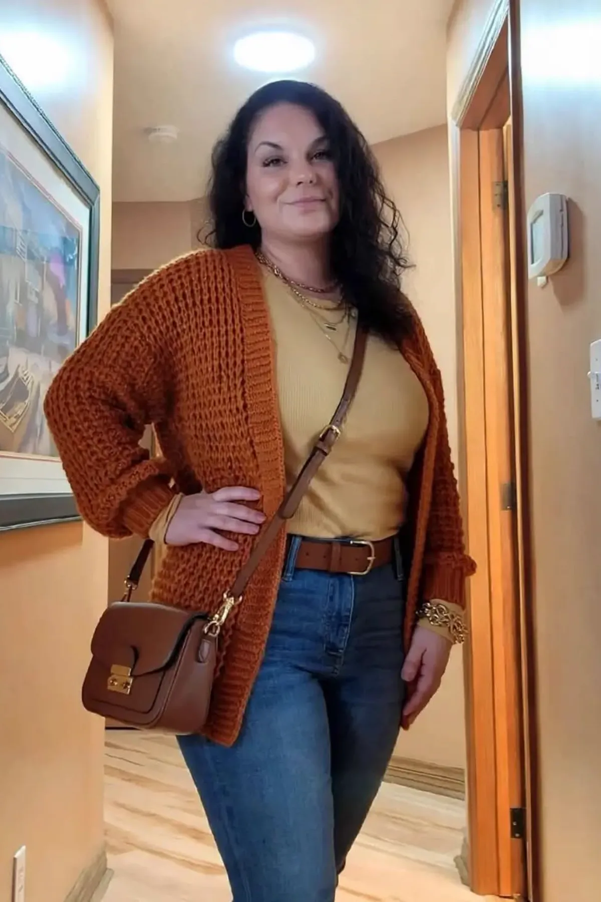 Woman in a burnt orange cardigan and black jeans with a witch hat, an easy plus size witch costume
