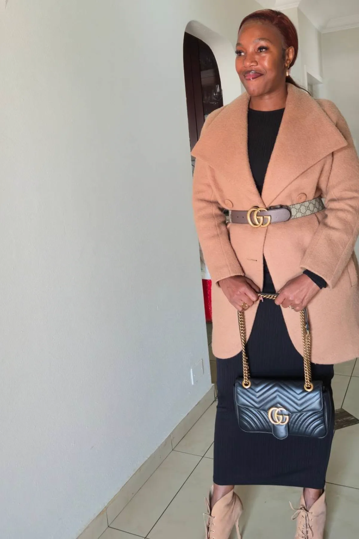 Woman in a camel coat and black knit dress with a feather hat, a plus size traveling witch costume